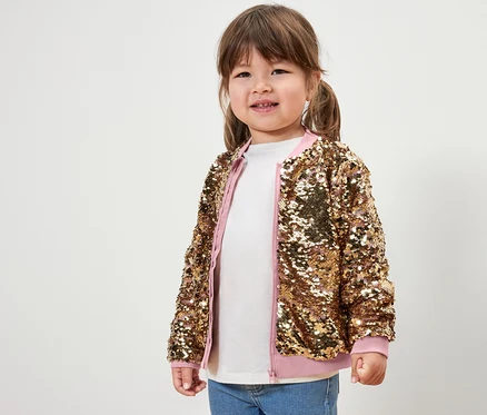 Une petite fille souriante pose en veste à paillettes pour enfants.