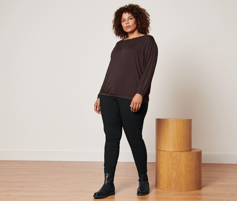 Femme posant dans un t-shirt manches chauve-souris marron, un pantalon stretch noir et des bottines en cuir.