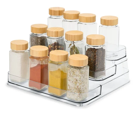 Sur un présentoir à épices transparent à trois niveaux, il y a 12 pots à épices en verre avec des couvercles en bois.