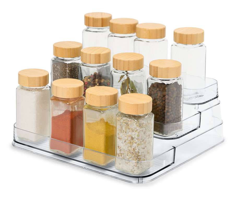 Sur un présentoir à épices transparent à trois niveaux, il y a 12 pots à épices en verre avec des couvercles en bois.
