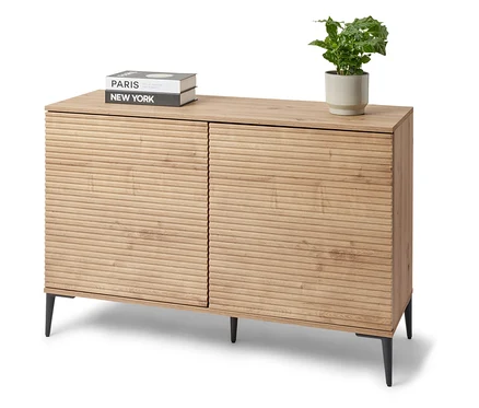 Un buffet « REET » avec aspect lamellé se trouve dans la pièce. Des livres et une plante en pot sont posés sur le buffet.
