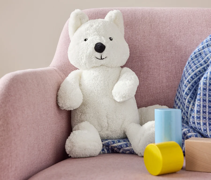 Un ours en peluche est assis sur un fauteuil rose à côté de blocs de bois et d'une couverture bleue.