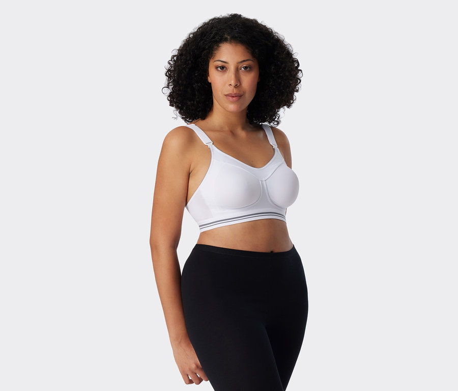 Une femme aux cheveux bouclés porte un soutien-gorge de sport blanc et un legging noir.