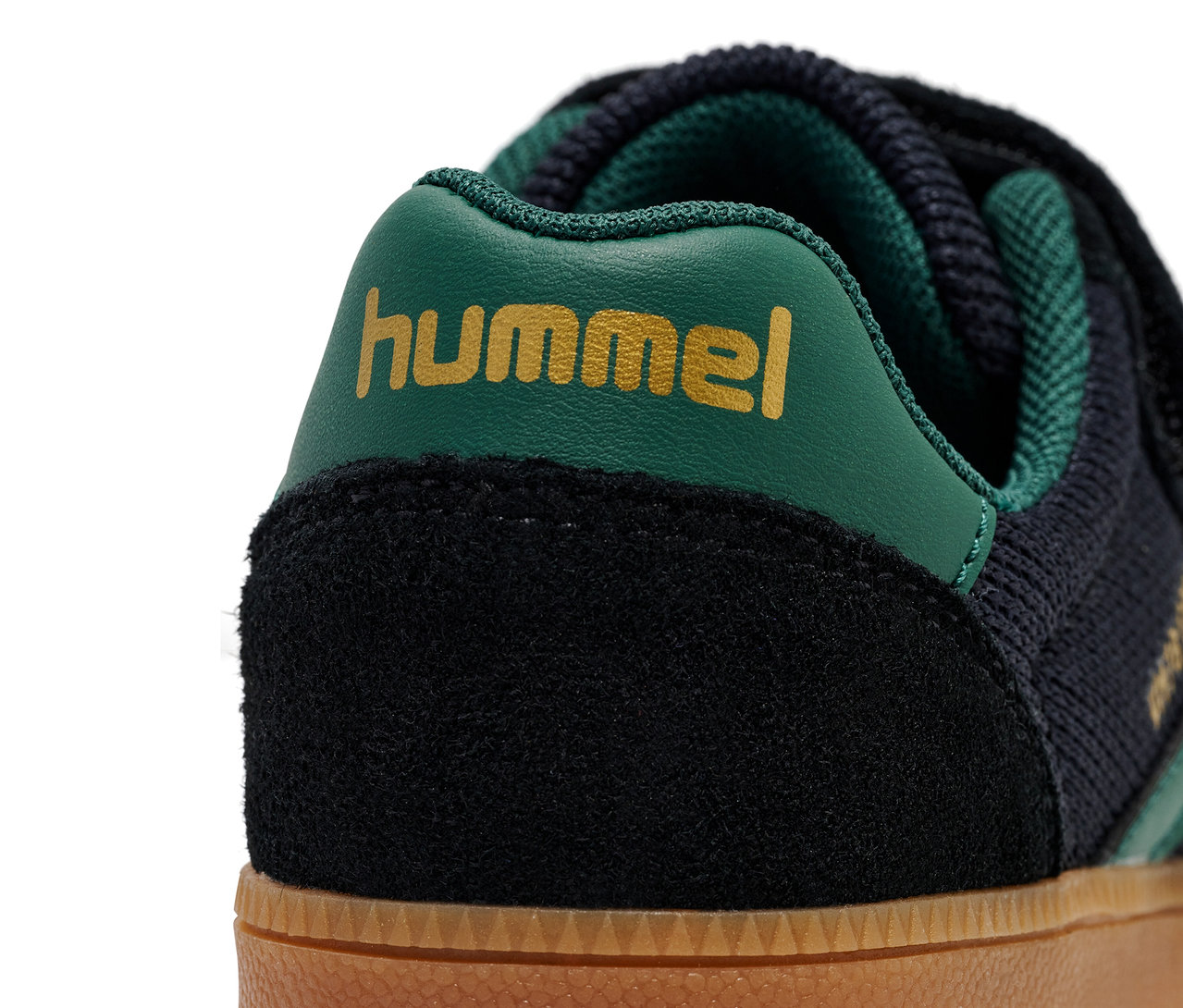 Gros plan d'une chaussure HUMMEL VM78 CPH JR avec du daim noir, du tricot bleu foncé et un logo vert.