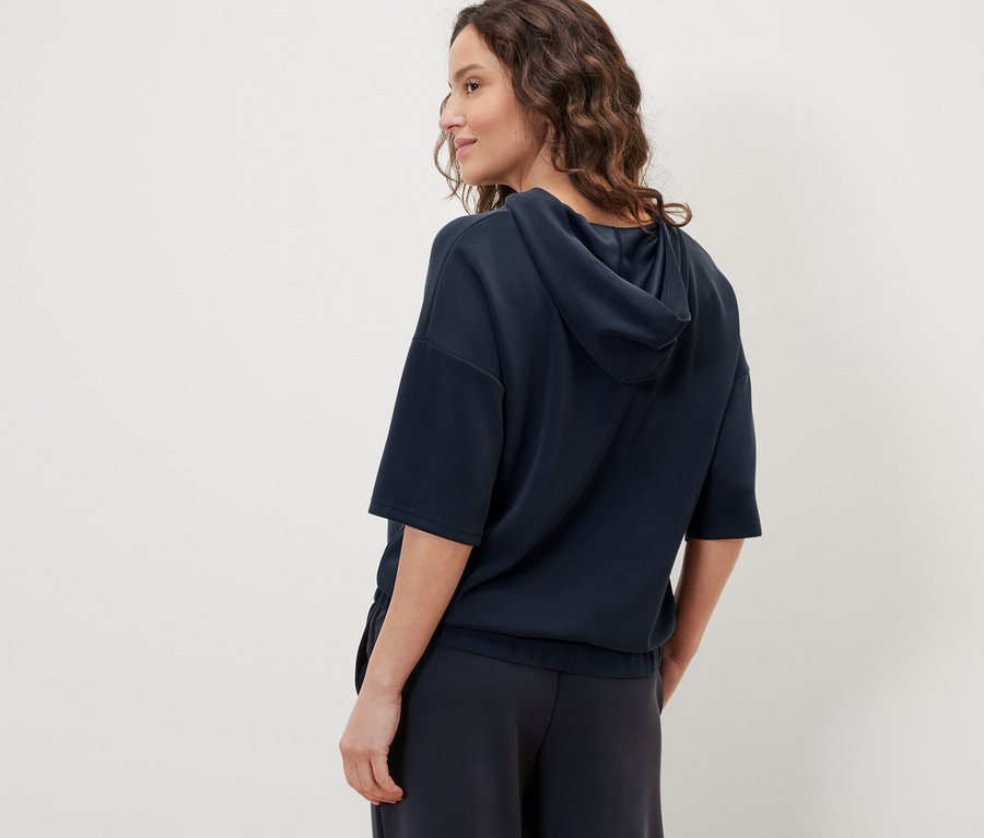 Une femme porte un pull à capuche bleu foncé en mélange de modal et un pantalon bleu foncé.