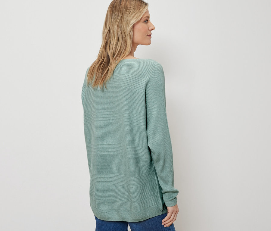 Femme posant en pull en maille fine, sauge, et jean bleu.