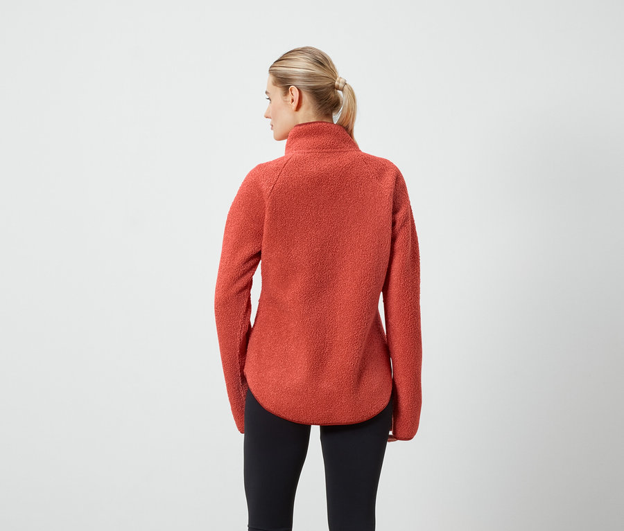 Une femme, vue de dos, porte un pull en polaire orange et un legging noir.