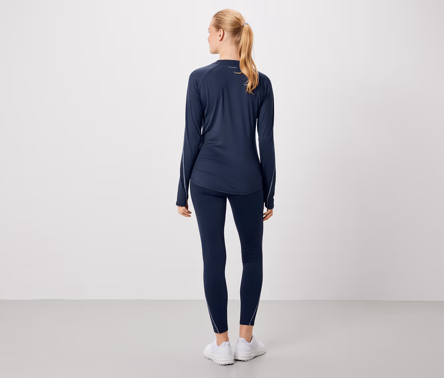 Une femme pose de dos en tenue de sport bleu marine et chaussures blanches.
