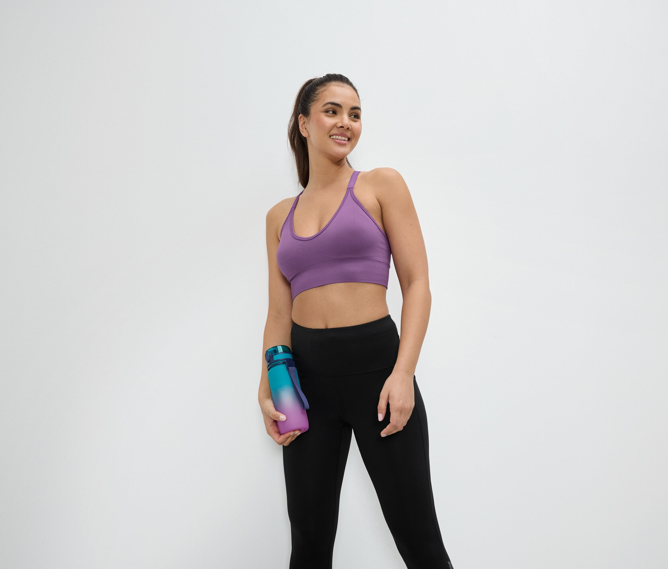 Femme en soutien-gorge de sport et leggings tenant une bouteille d'eau.