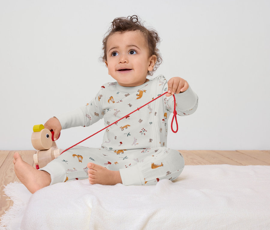 Un bébé est assis sur une couverture blanche et joue avec un jouet à tirer en bois.