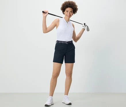 Une femme tient un club de golf sur ses épaules et porte un short technique en softshell bleu foncé.