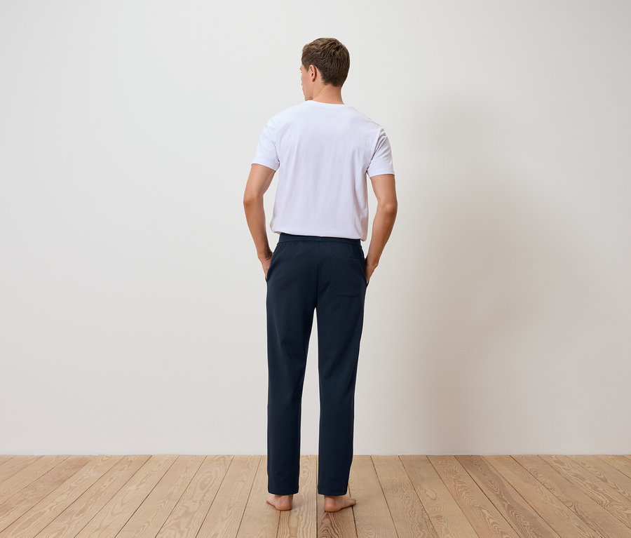 Un homme, dos à la caméra, porte un t-shirt blanc et un pantalon bleu marine.