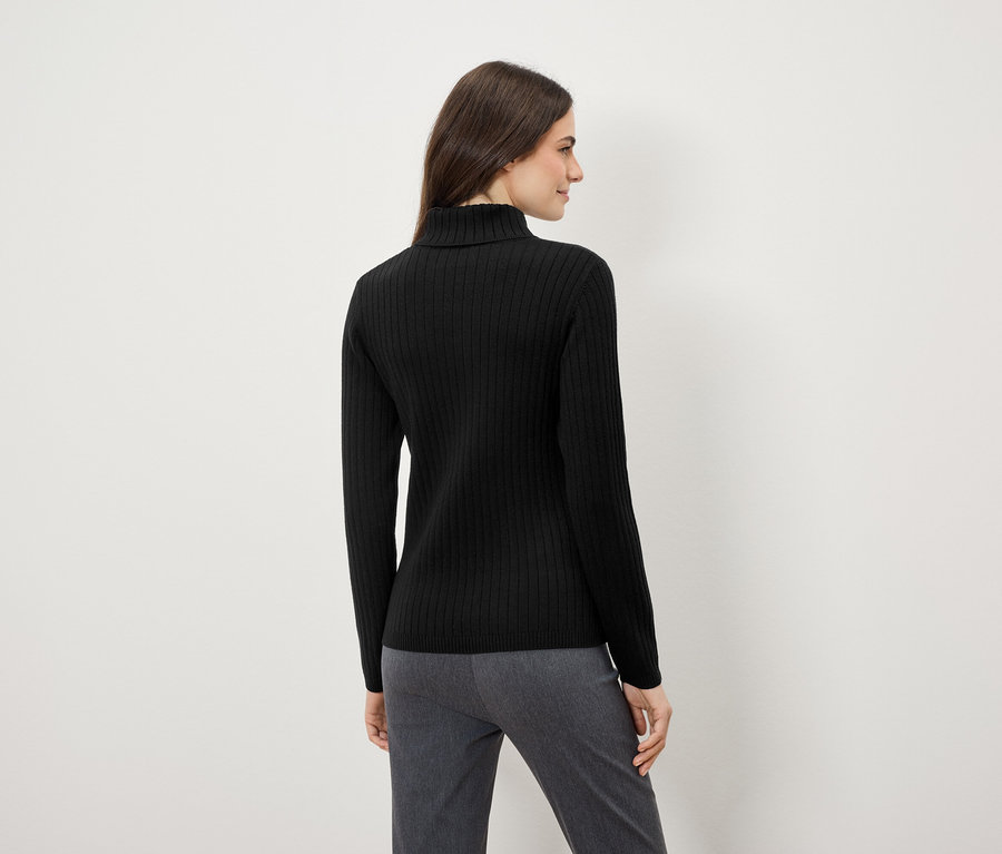 Femme portant un pull à col roulé noir et un pantalon gris, dos à la caméra.