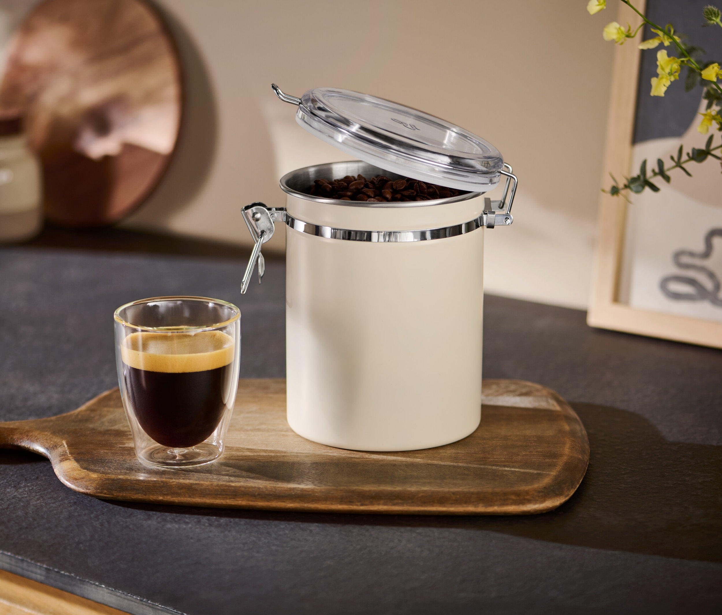 Boîte à arômes beige ouverte à côté d'une tasse d'expresso sur un plateau en bois.