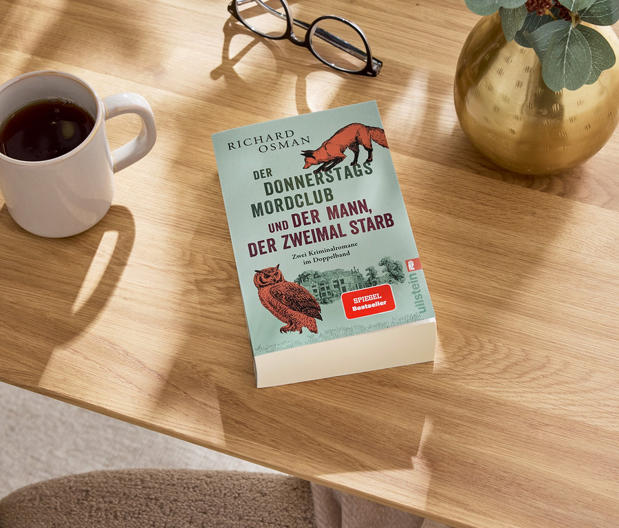 Sur une table, il y a un livre, une tasse avec une boisson, des lunettes et un vase.