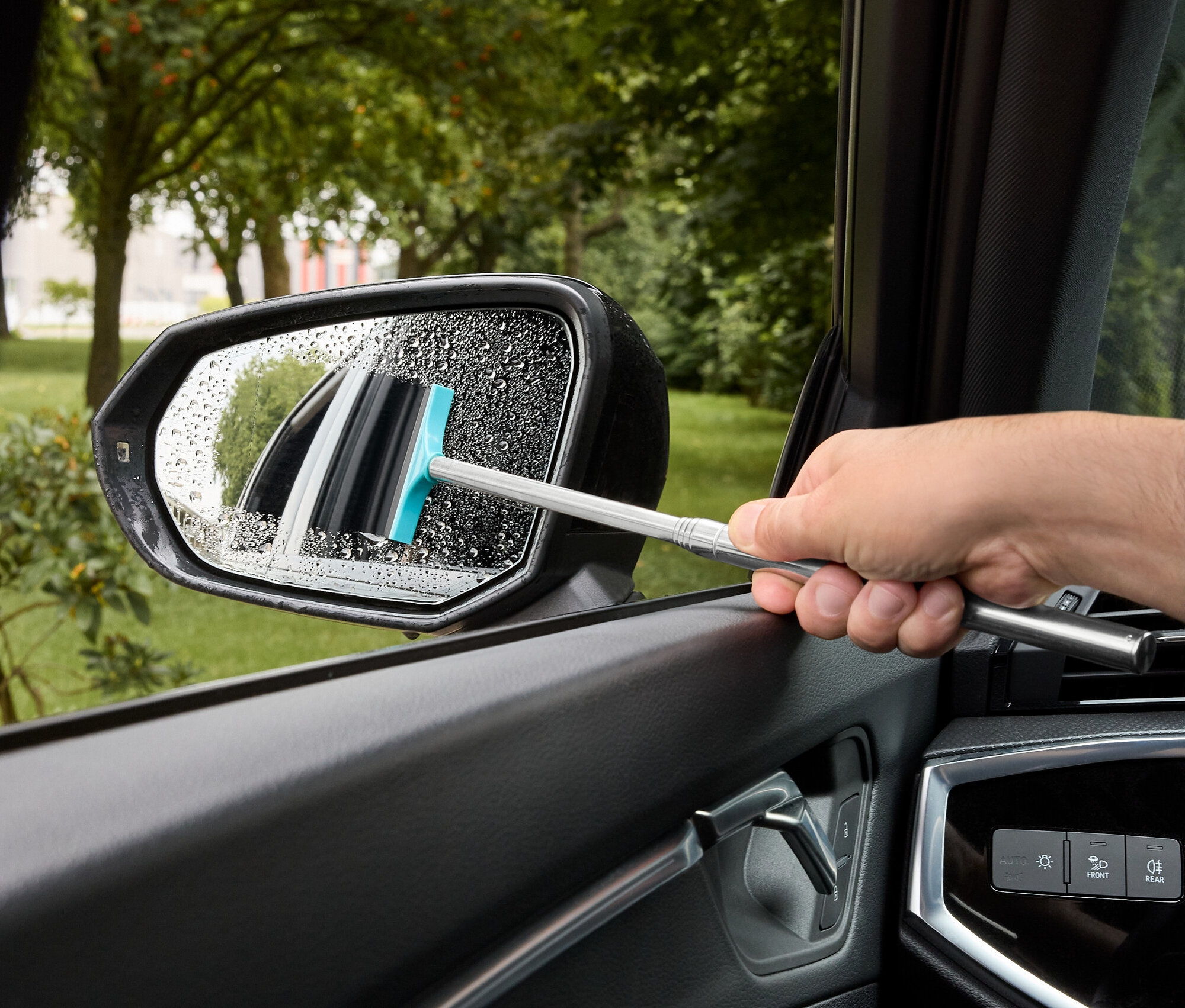 Un homme essuie l'eau d'un rétroviseur de voiture avec une raclette à caoutchouc bleu.