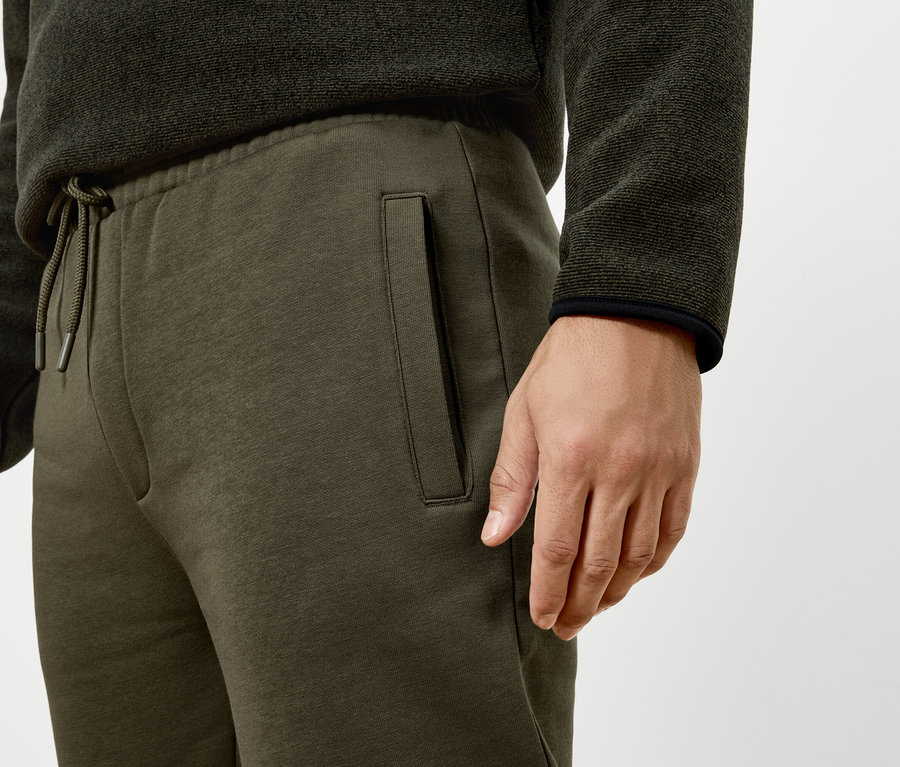 Un homme porte un pantalon de survêtement vert et un pull.