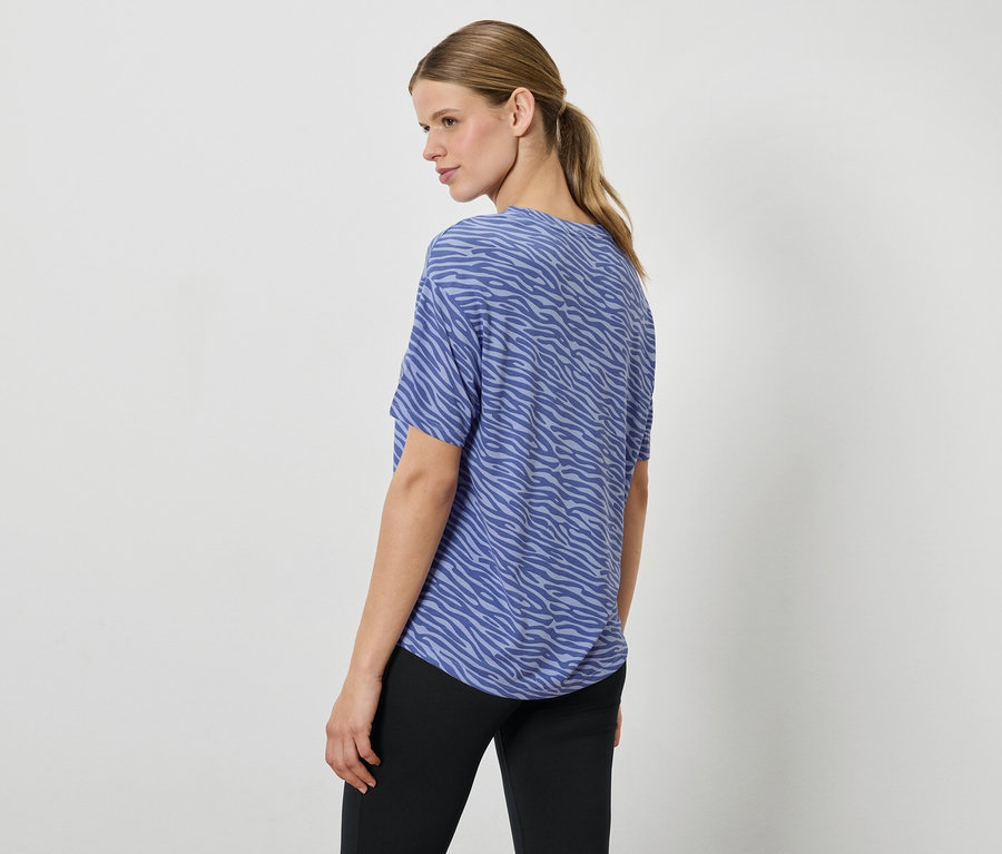 Une femme portant un haut bleu à motif animalier et un pantalon noir, regardant par-dessus son épaule.