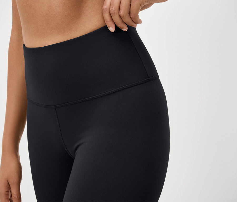 Gros plan d'une femme portant des leggings noirs taille haute et ajustant la ceinture.