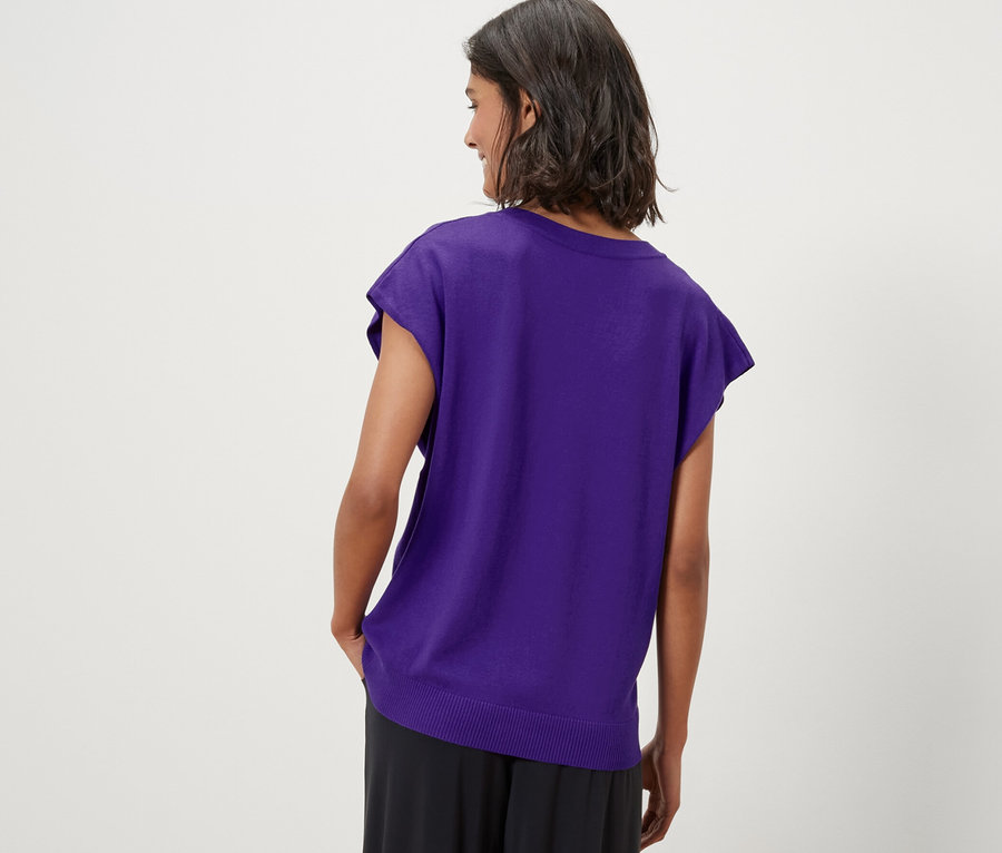 Une femme porte un pull-over violet en maille fine à manches courtes.