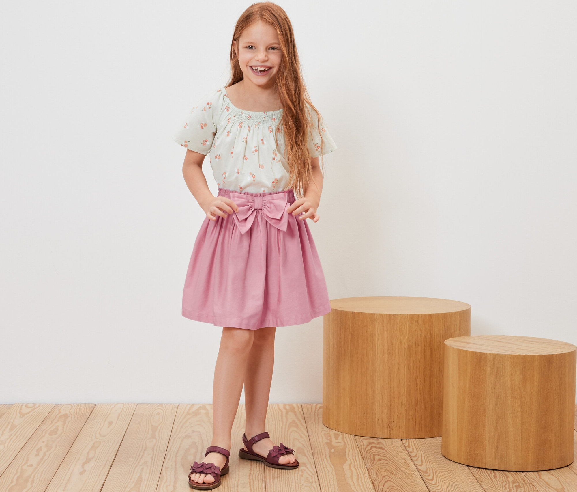 Fillette rousse souriante posant en jupe tissée pour enfant et haut fleuri.