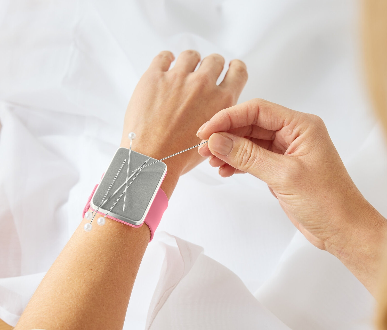 Une femme coud du tissu avec un Armnadelkissen, magnétique, sur son poignet.