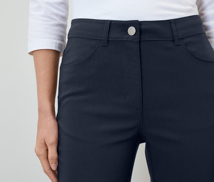 Une femme porte un pantalon bleu marine et une chemise blanche.