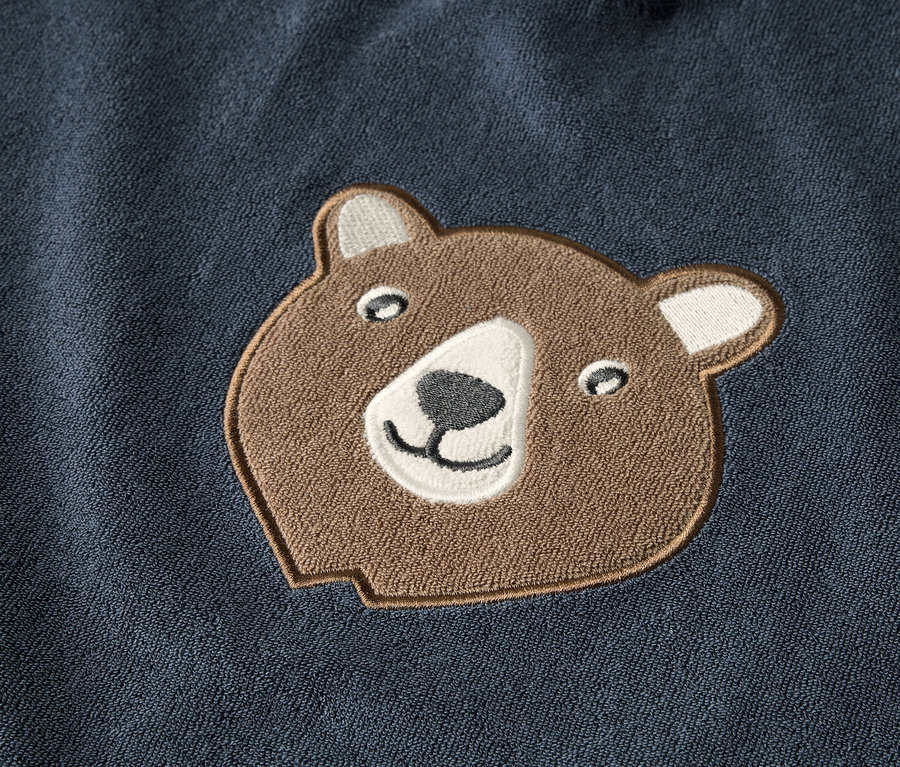 Détail d'un poncho en tissu éponge pour enfant avec un patch tête d'ours brun.