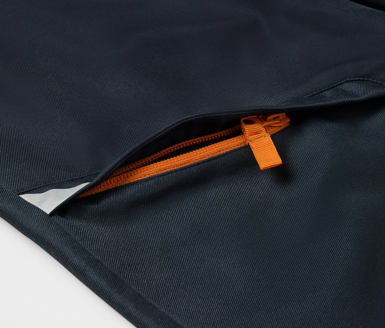 Gros plan sur un pantalon en softshell pour enfant avec une fermeture éclair orange sur la poche.