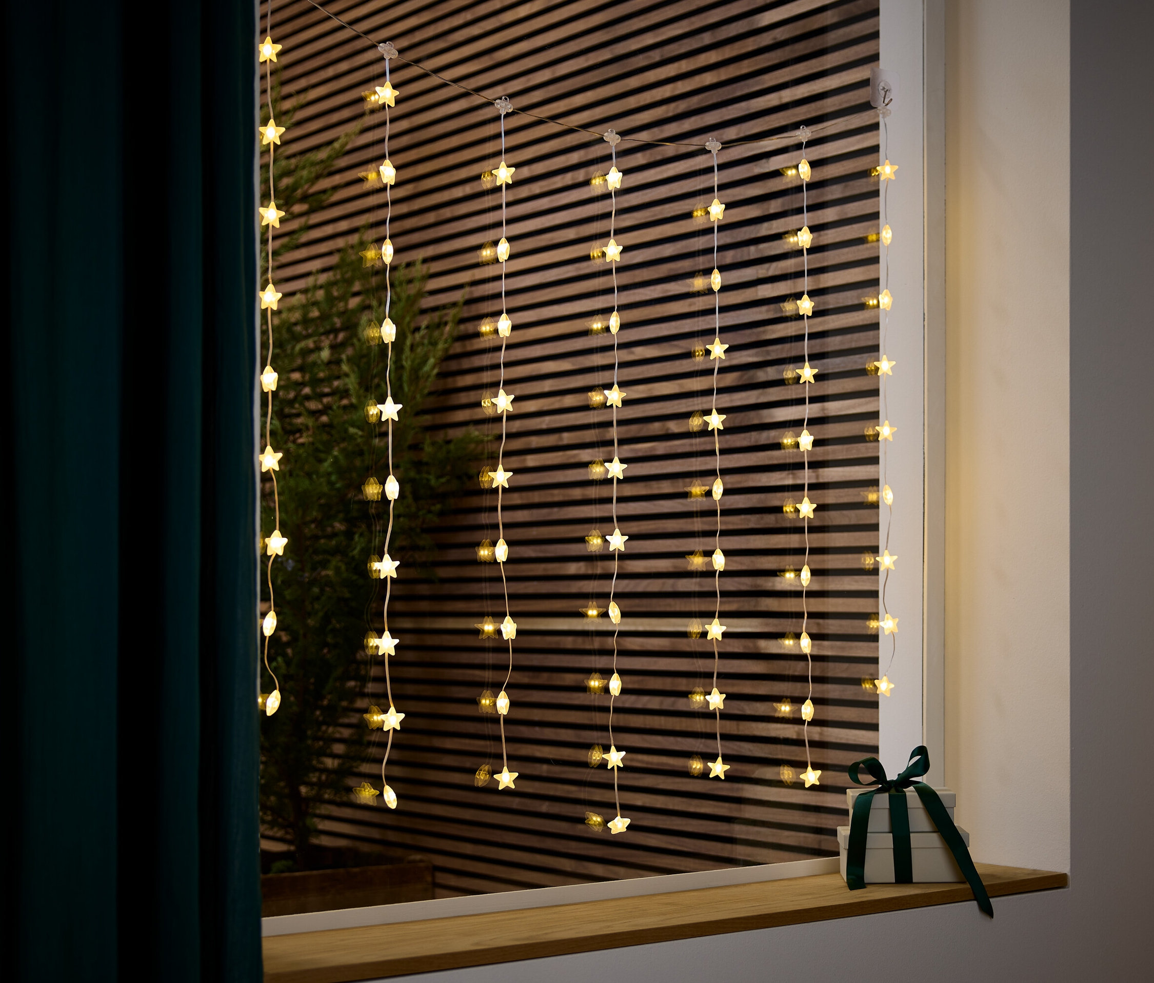 Une guirlande lumineuse à étoiles est suspendue à une fenêtre à côté d'un cadeau avec un ruban vert foncé.
