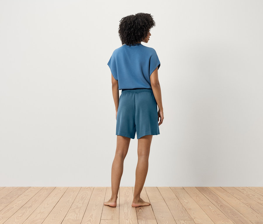 Une femme en t-shirt bleu et short, de dos.