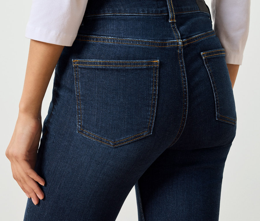Gros plan d'une femme vue de dos portant un jean bleu foncé avec des poches et des coutures marron.