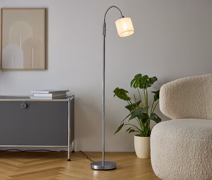 Intérieur avec une commode grise, un vase avec des fleurs séchées, deux livres, une lampe argentée et un fauteuil crème.