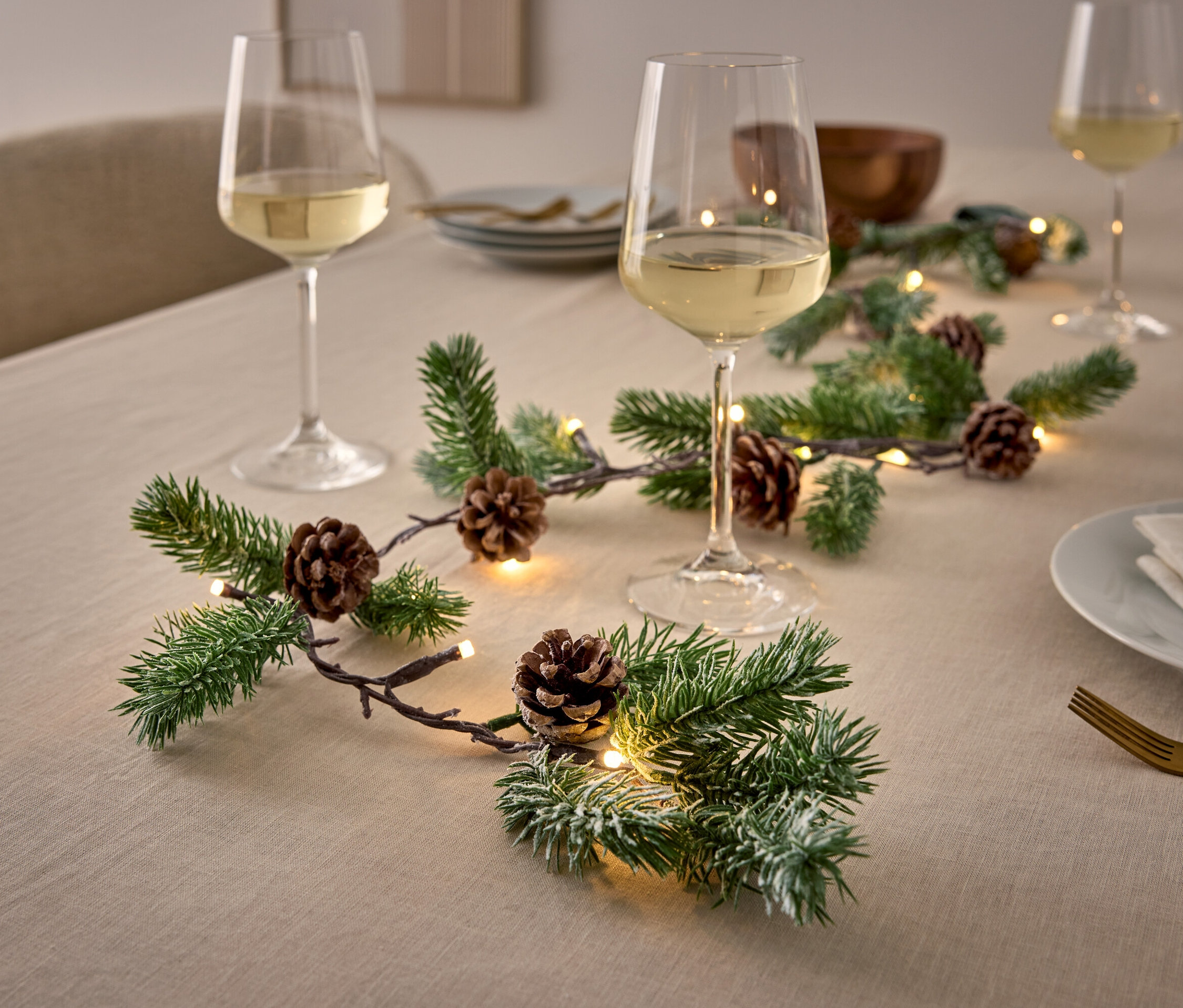 Table décorative avec des branches, des pommes de pin, des lumières et des verres à vin.