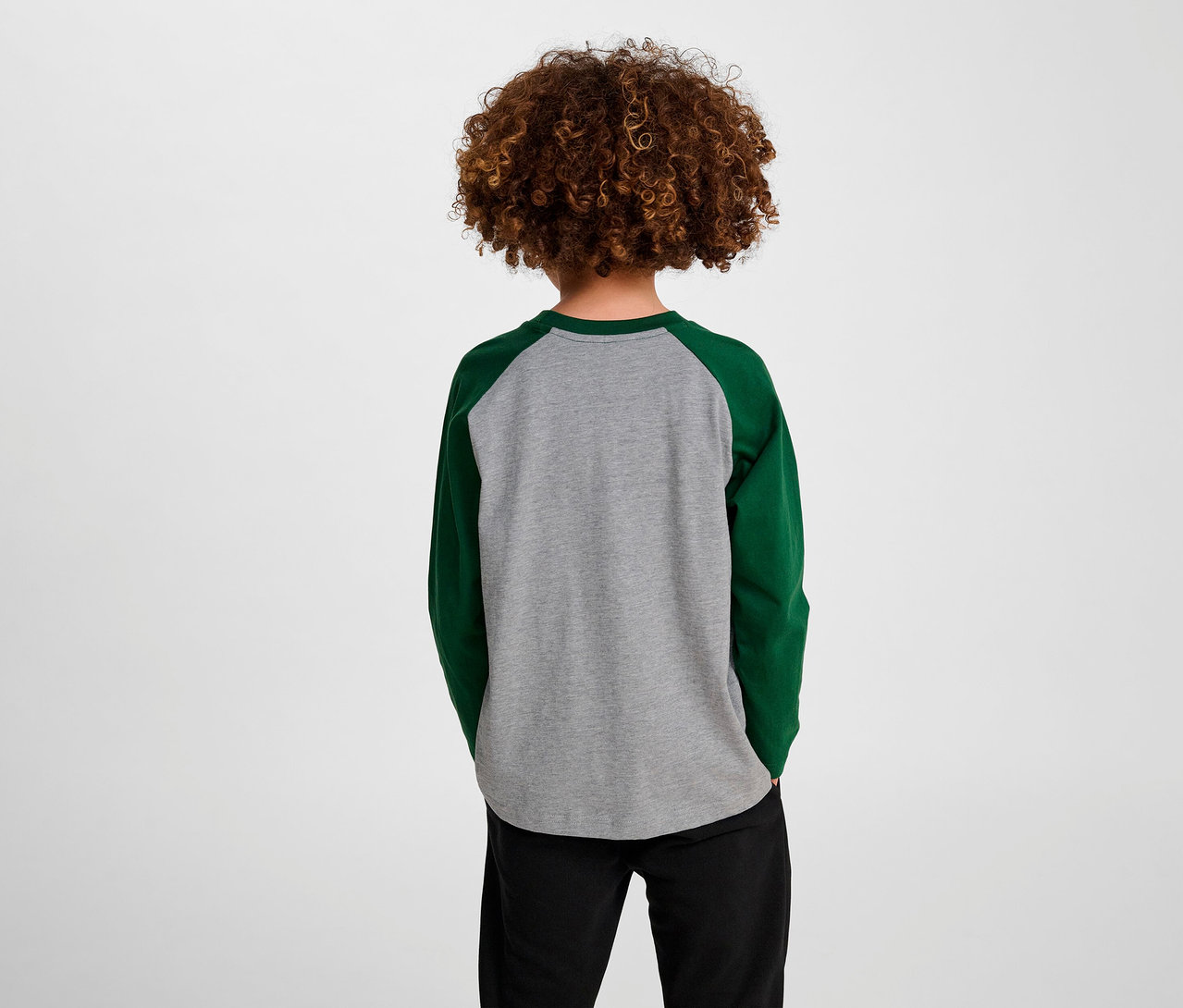 Garçon aux cheveux bouclés, vu de dos, portant un T-shirt ample à manches raglan HUMMEL HMLJR BEE vert.