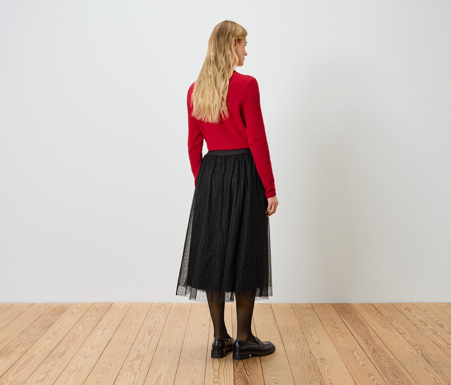 Une femme dos à la caméra porte un pull rouge et une jupe noire.