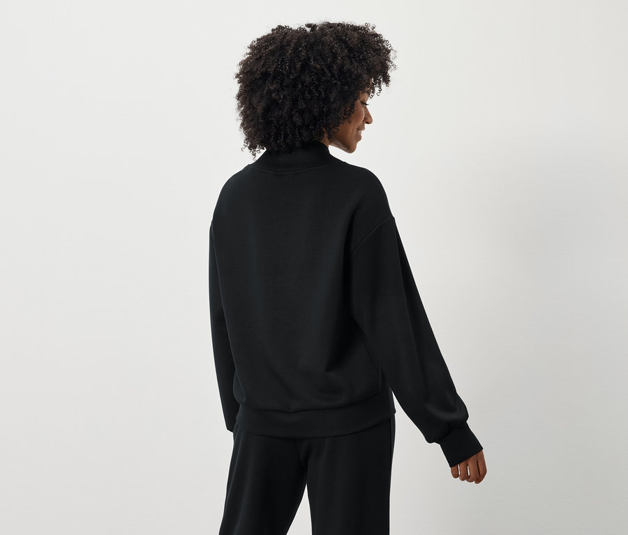 Vue arrière d'une femme aux cheveux bouclés portant un pull et un pantalon noirs.