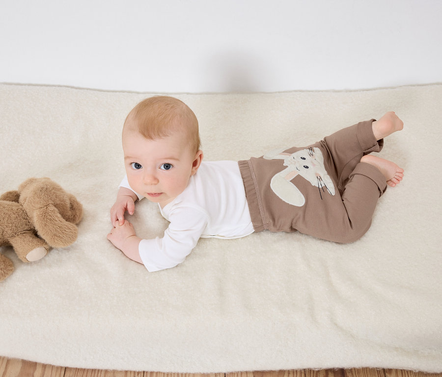 Un bébé est allongé sur le ventre sur une couverture blanche à côté d'un éléphant en peluche.