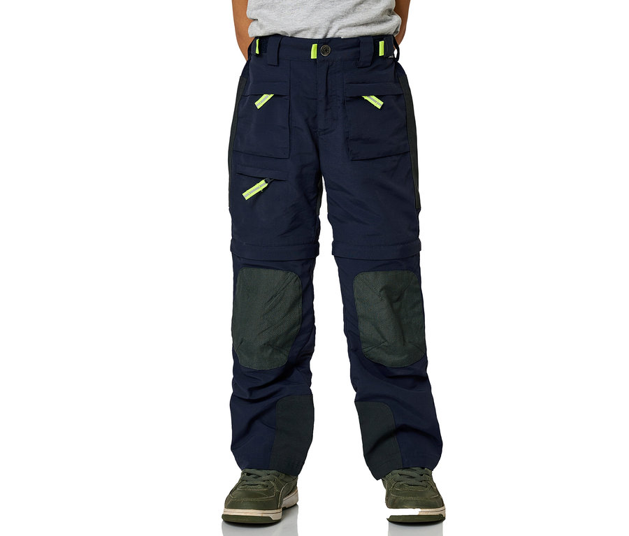 Enfant portant un pantalon zipp-off JAKO-O marine avec des accents jaune fluo sur les poches, des renforts foncés aux genoux et des baskets vert olive.