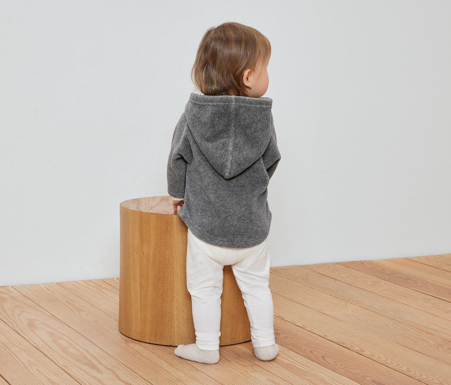 Bébé debout, vu de dos, portant une veste en polaire grise pour bébé.