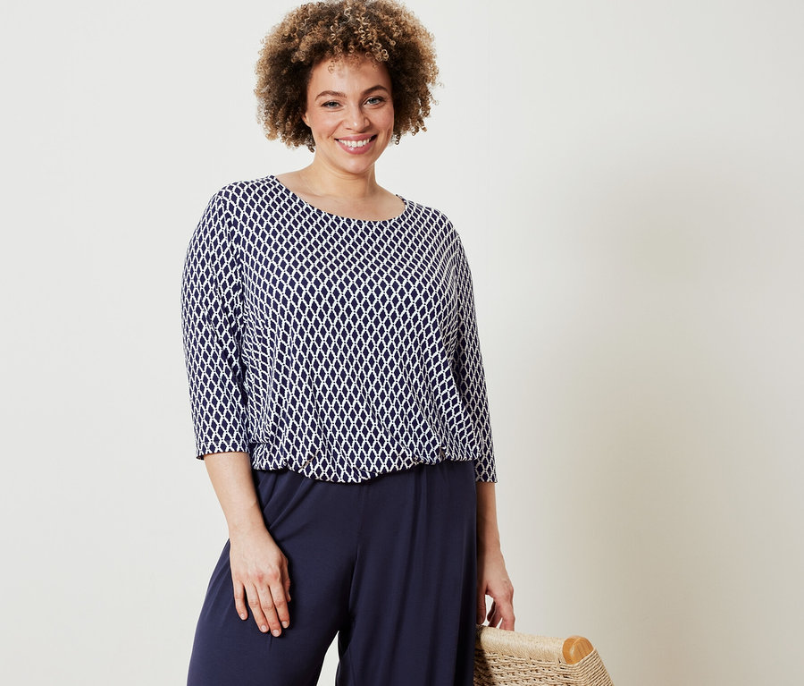 Femme posant dans un chemisier imprimé et un pantalon palazzo bleu foncé.