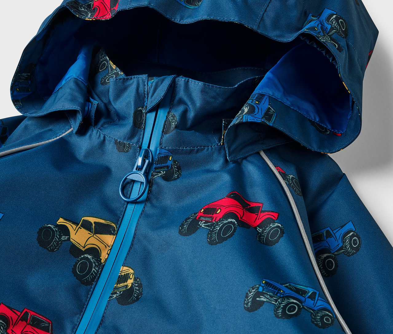 Détail d'une veste imperméable thermique pour enfants avec un motif de monster trucks.