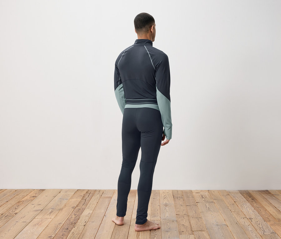 Un homme vu de dos portant des vêtements thermiques gris foncé sur un plancher en bois.