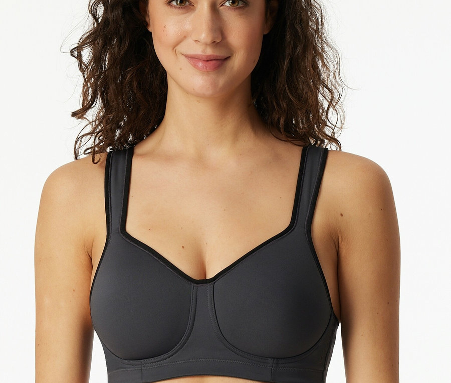 Une femme souriante porte un soutien-gorge de sport gris.