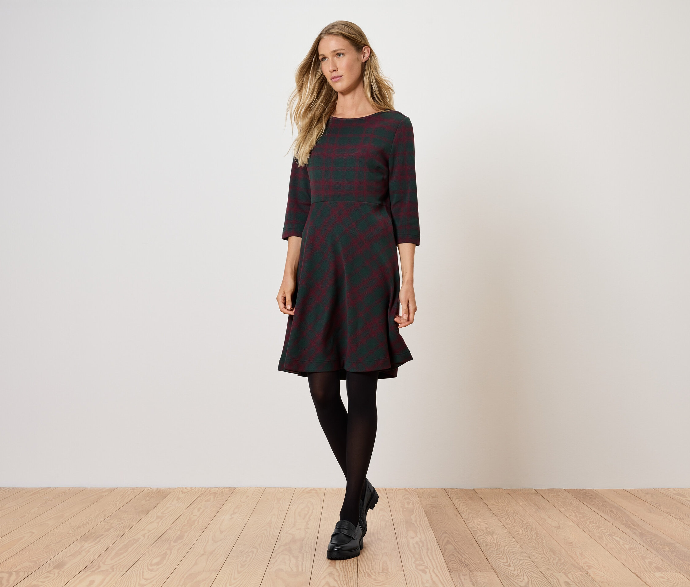 Femme posant dans une robe grise à manches trois-quarts et des collants noirs.