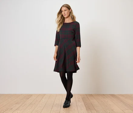 Femme posant dans une robe grise à manches trois-quarts et des collants noirs.