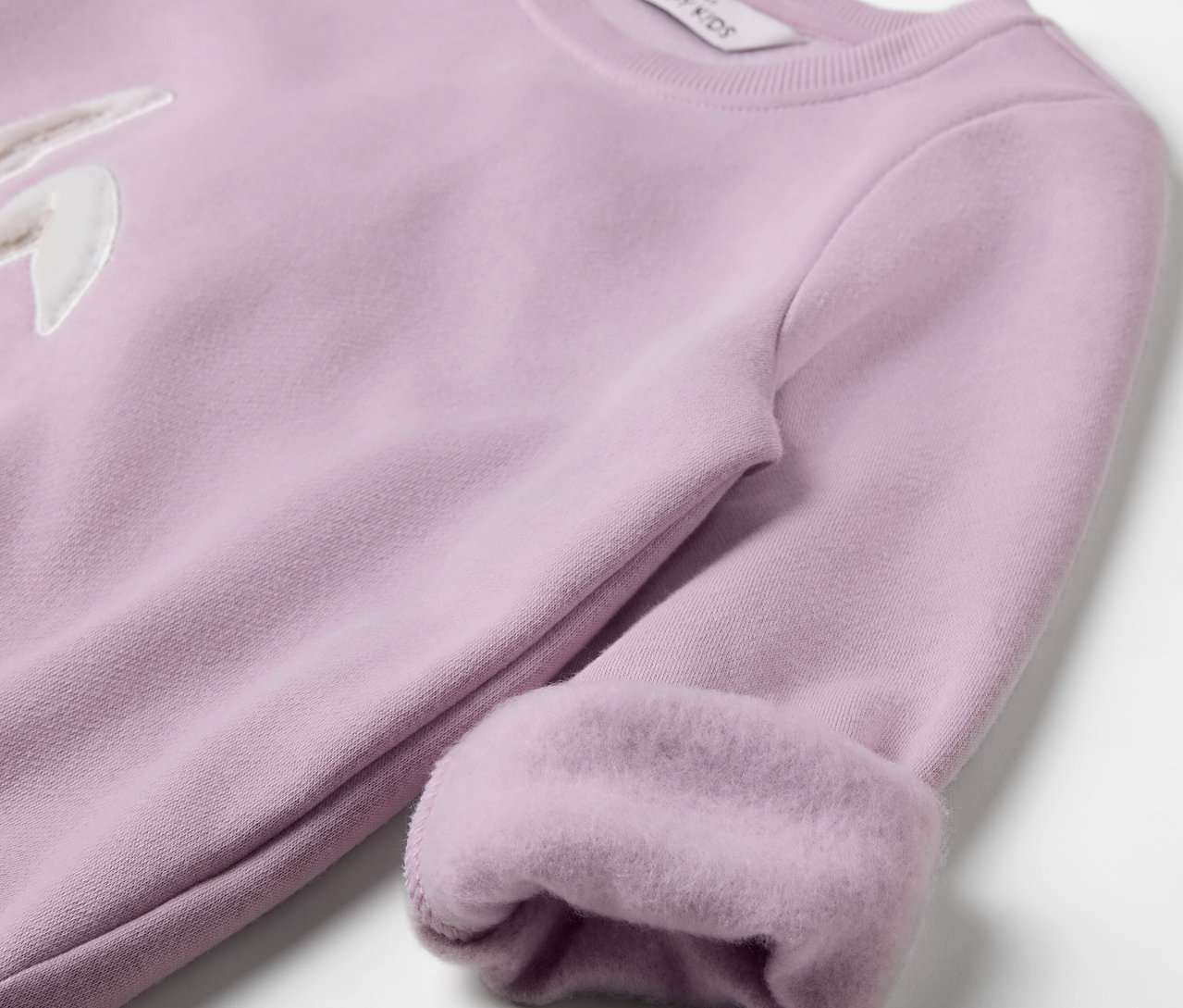 Gros plan sur un sweat-shirt lilas clair avec un appliqué lapin et des manches retroussées.