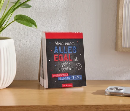 Calendrier de table avec l'inscription "Quand TOUT est ÉGAL à quelqu'un, ça se passe en fait en 2026", à côté d'un pot de fleurs et d'un téléphone portable sur la table.