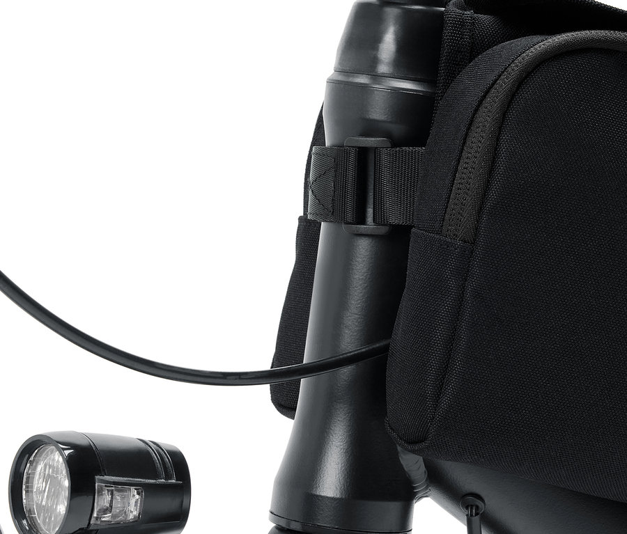 Gros plan du guidon d'un vélo avec une lampe et un sac noir.