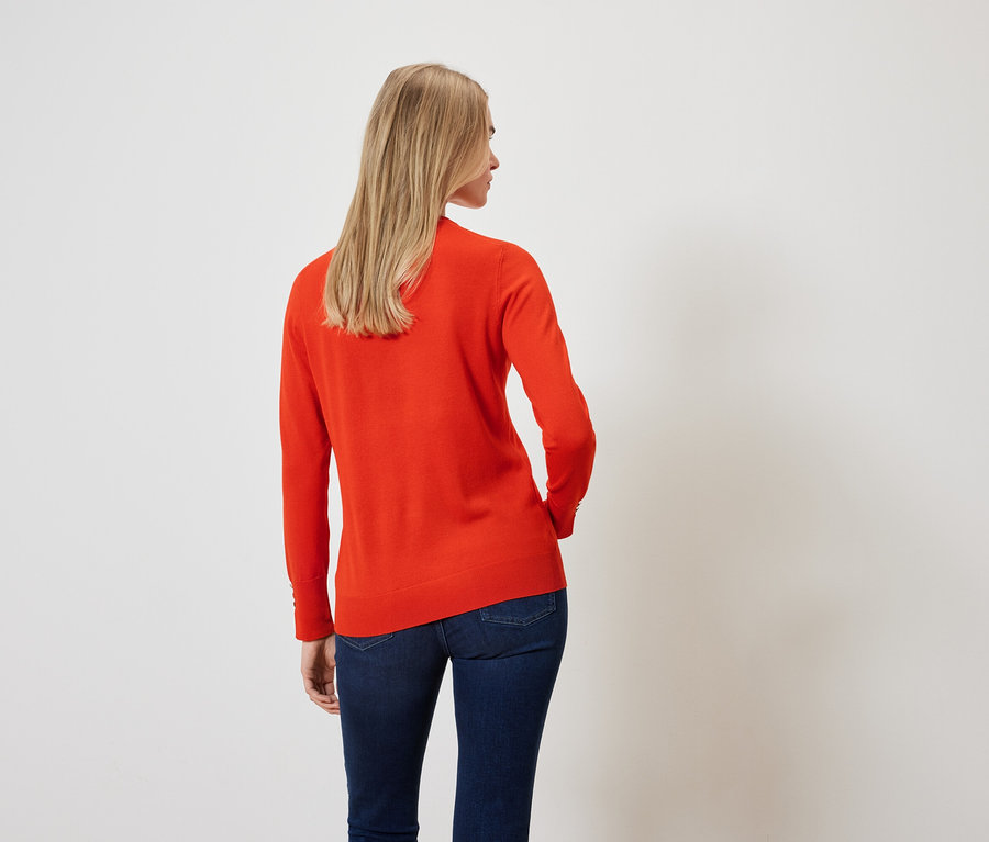 Vue arrière d'une femme blonde portant un pull orange et un jean bleu foncé.